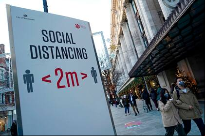 Los peatones que llevan una máscara facial o se cubren debido a la pandemia de COVID-19, pasan por un letrero que pide a las personas que se alejen socialmente, en Oxford Street, en el centro de Londres.