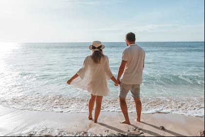 man and a girl hold hands and watch the sunset on the beach