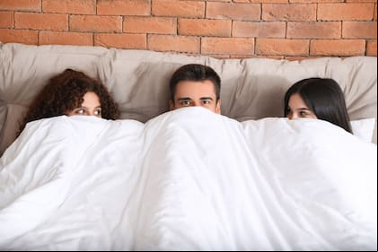 Man with two beautiful women in bed. Polyamory concept