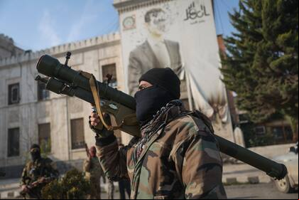 Un combatiente de la oposición siria sostiene un lanzacohetes ante una oficina gubernamental, con la imagen del derrocado presidente Bashar Assad con varios balazos en la fachada