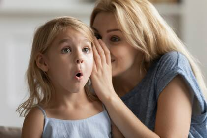 Young mother whisper in surprised cute little daughter ear tell secret, millennial mom or nanny play with small preschooler girl child, share close intimate moment at home, gossip or chat together
